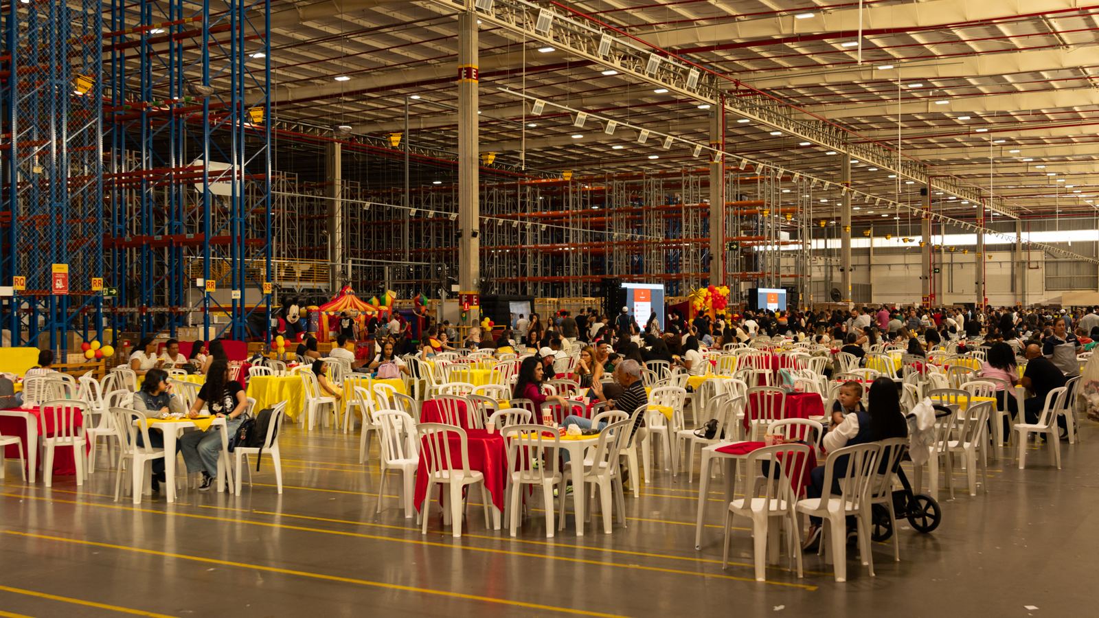 Dia da Família corporativo montado dentro do centro de distribuição da empresa, com centenas de colaboradores e familiares nas mesas